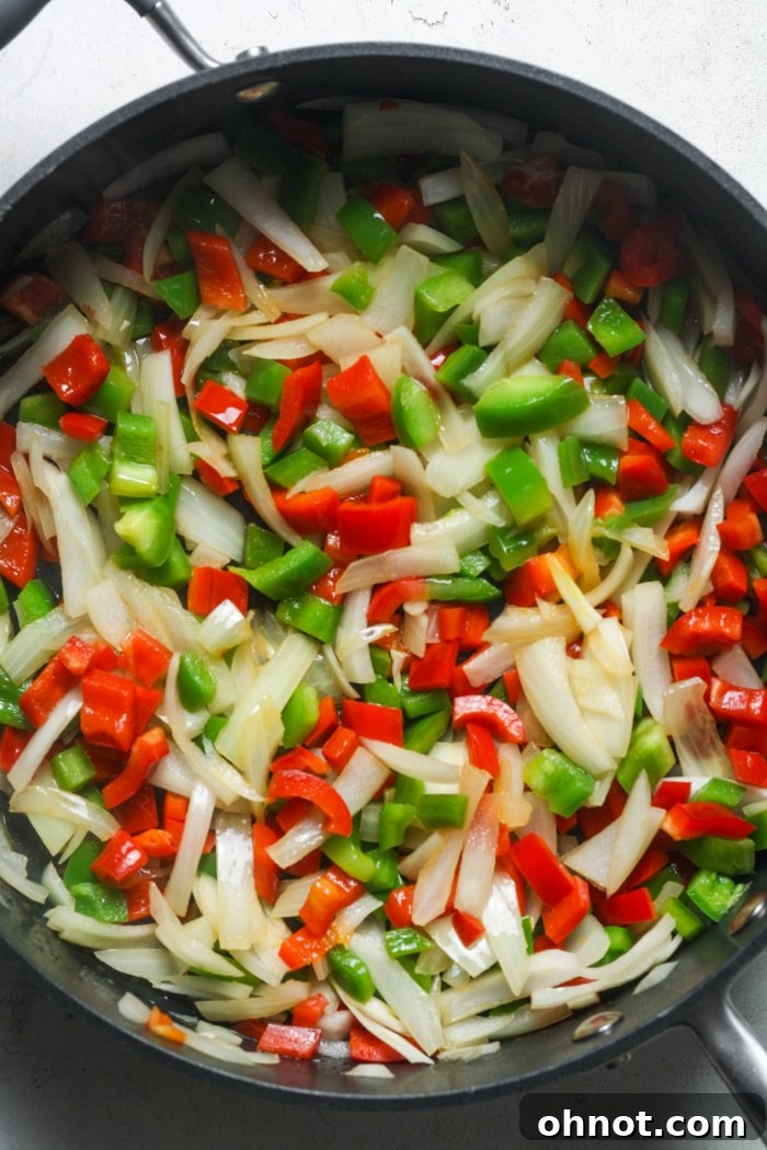 Chopped onions and colorful bell peppers sautéing in olive oil in a large skillet.