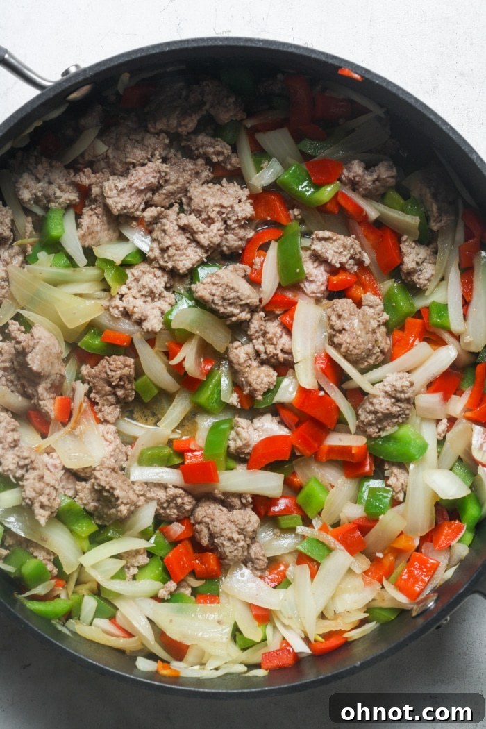 Ground meat cooking in a skillet with sautéed bell peppers and onions, browning nicely.