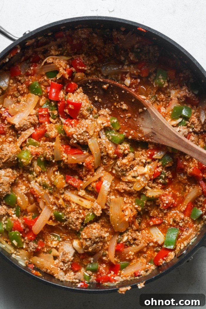 All ingredients, including ground meat, peppers, onions, tomato sauce, and rice, simmering together in a large skillet.