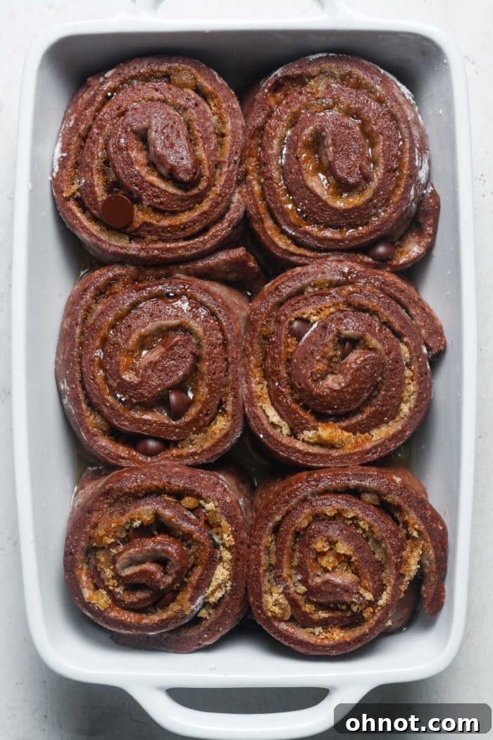 Risen chocolate cinnamon rolls in a baking pan.