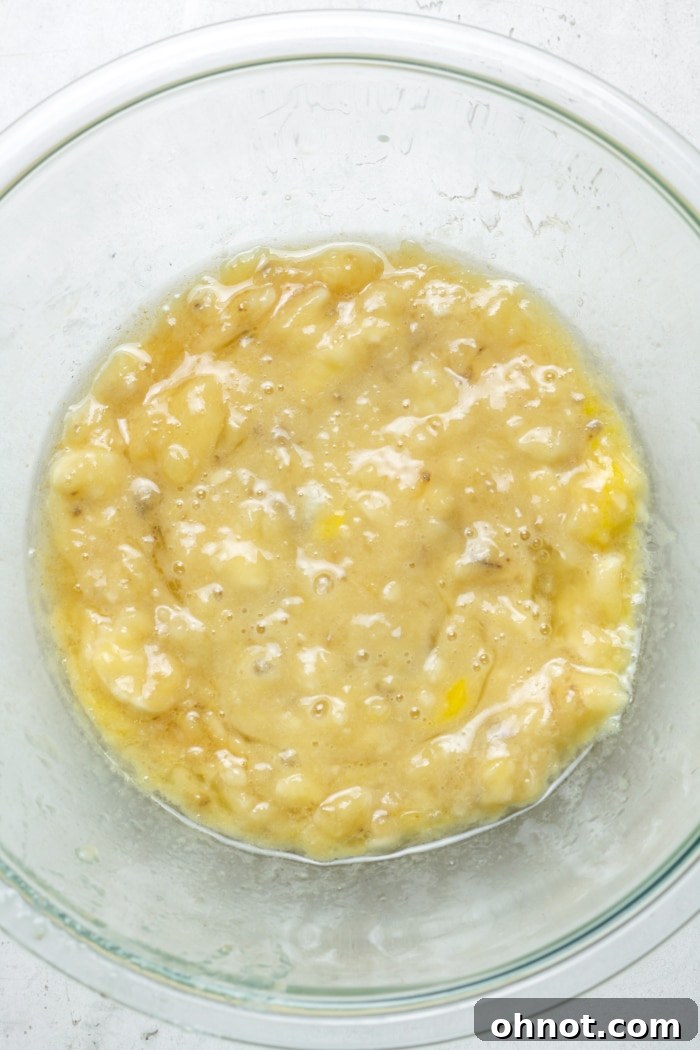 Mashed ripe bananas, egg, coconut oil, and vanilla extract mixed in a bowl.