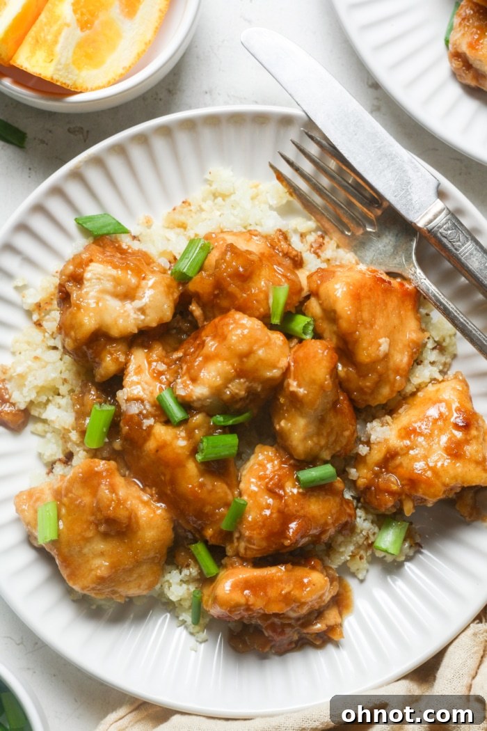 Delicious gluten-free orange chicken served with rice, garnished with fresh green onions and sesame seeds.