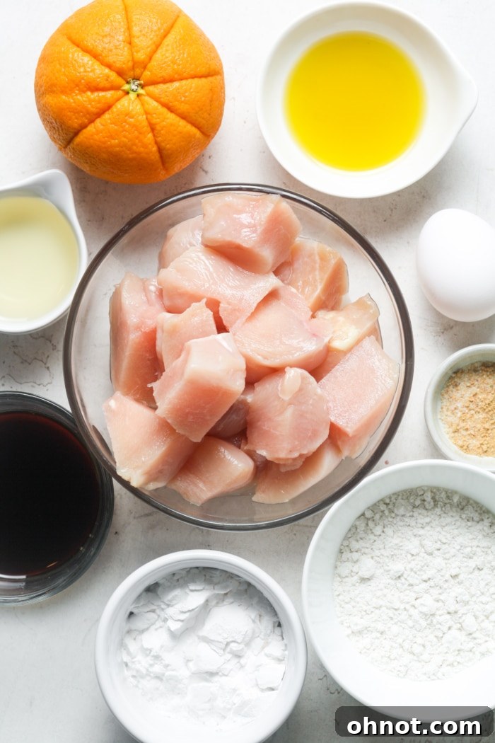 A vibrant selection of fresh ingredients including oranges, ginger, garlic, and chicken, ready for making gluten-free orange chicken.