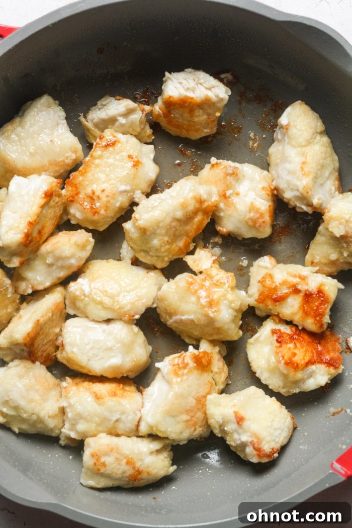 A large skillet filled with golden-brown cubed chicken pieces, actively cooking in hot oil to achieve a perfect crispy texture.