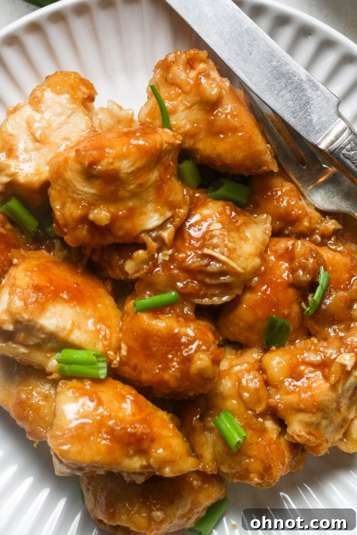 Close-up view of succulent Chinese-style chicken generously coated in a glossy orange sauce, glistening under the light.