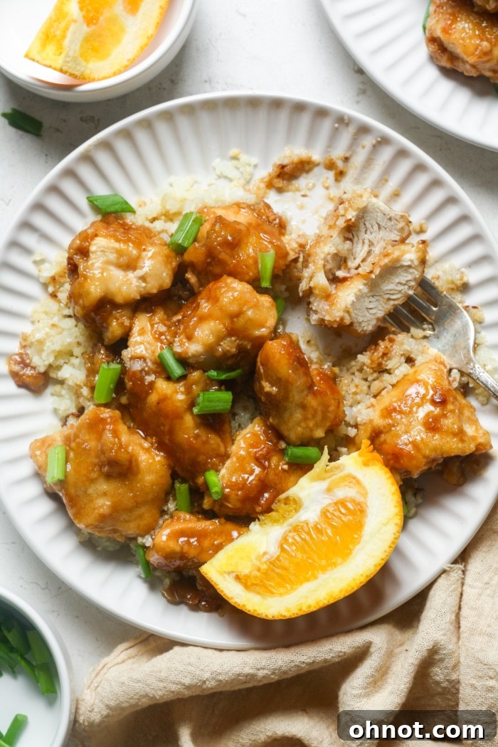 A close-up shot of crispy chicken pieces covered in a delectable orange sauce, with subtle garnishes of fresh green onions.