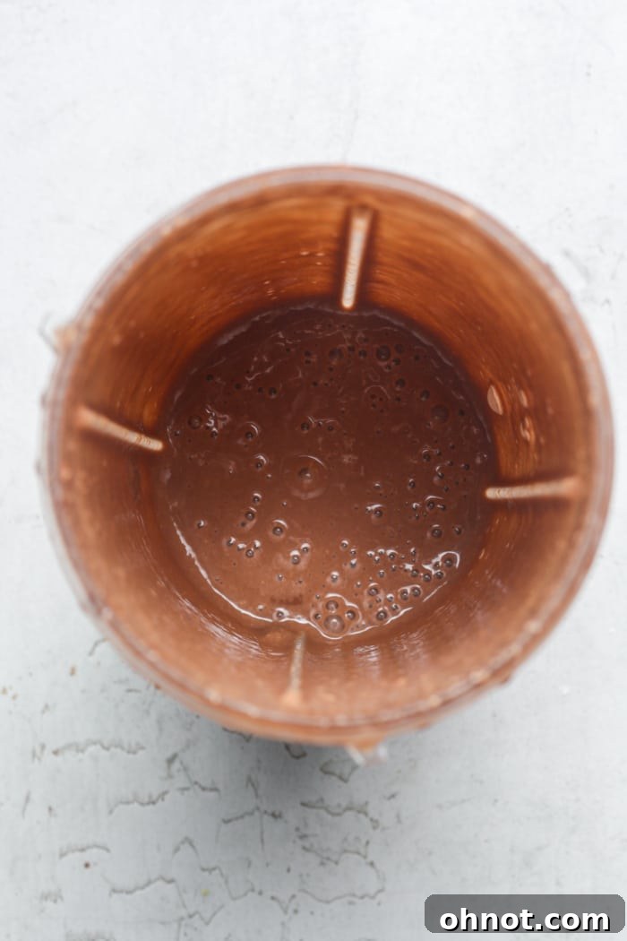 A close-up of a blender jar containing a smooth, creamy chocolate-colored batter for baked oats.