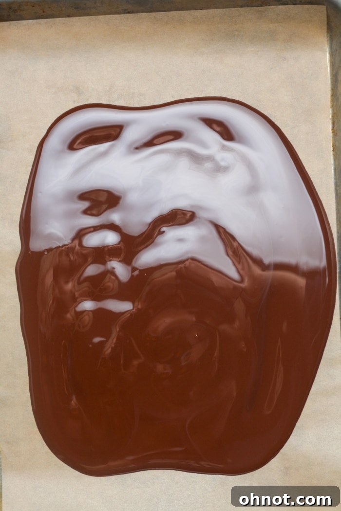 Smooth, melted chocolate spread evenly on parchment paper on a baking sheet, ready for toppings.
