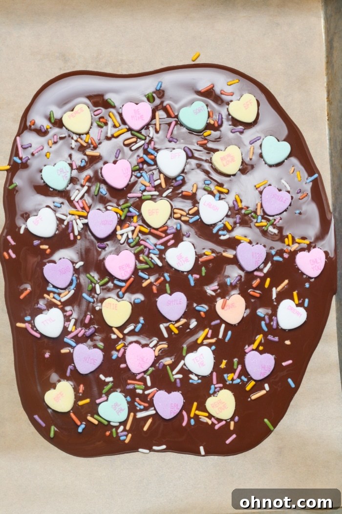 Melted chocolate generously topped with vibrant sweetheart candies and colorful sprinkles, creating a festive Valentine's design.