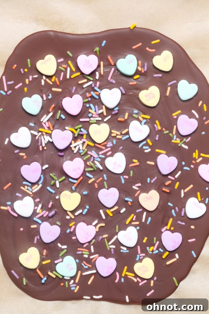 A sheet of hardened chocolate bark, adorned with a festive arrangement of Valentine's candies and sprinkles, perfectly set on a baking sheet.