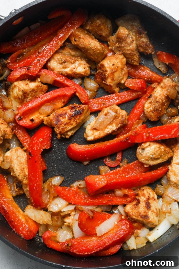 Colorful bell peppers, onions, and chicken cooking together in a skillet.