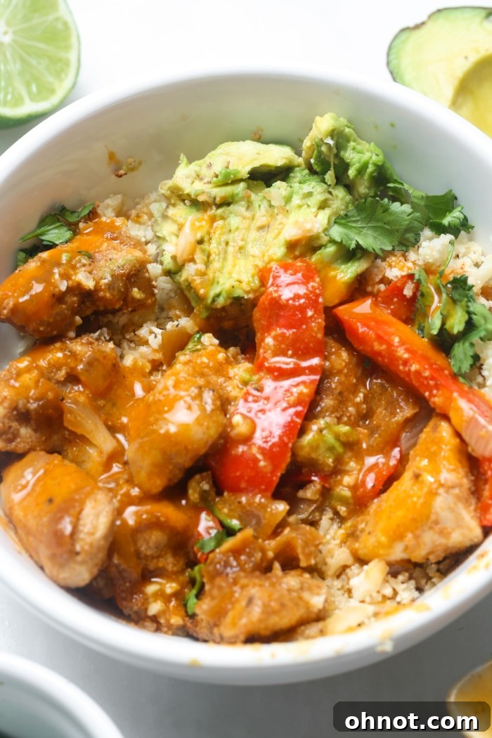 A perfectly assembled bowl of chicken, peppers, and onions with fresh toppings.