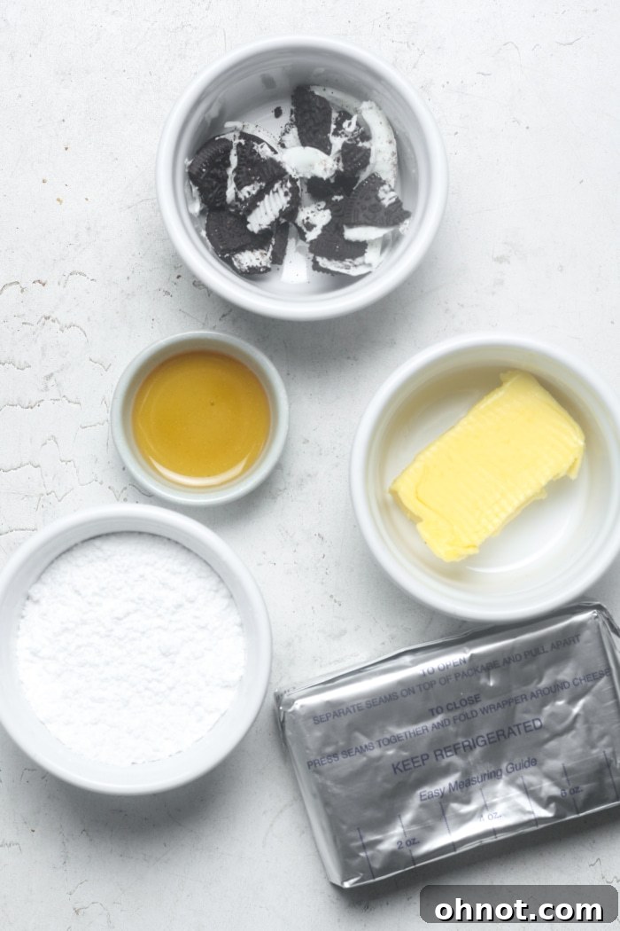 All the essential ingredients for making Oreo dip laid out on a white surface: cream cheese, butter, powdered sugar, vanilla extract, and a stack of Oreo cookies.