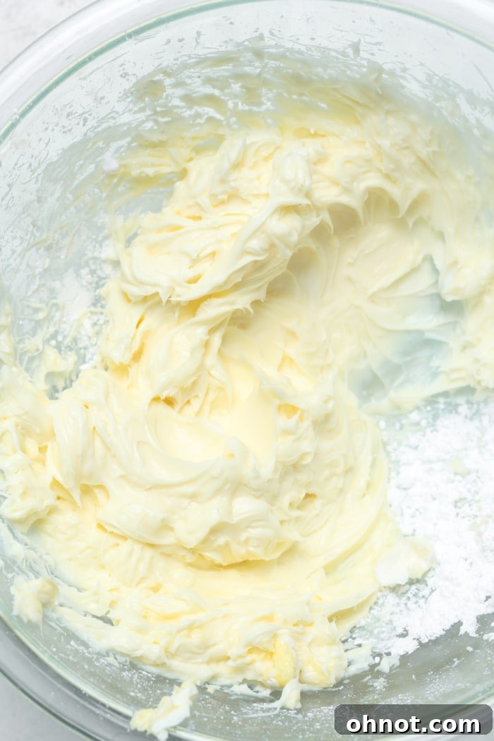 A mixing bowl showing beaten cream cheese, butter, and powdered sugar, looking smooth and creamy.