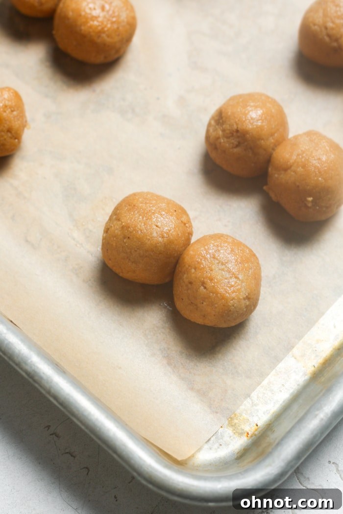 Two small, round cookie dough balls gently touching on a parchment-lined baking sheet.