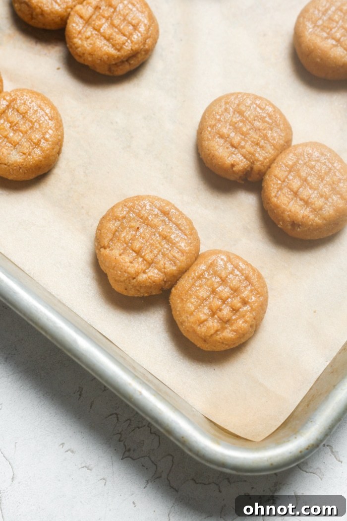 Cookie dough balls on a baking sheet, each pressed with a fork to create a criss-cross pattern.