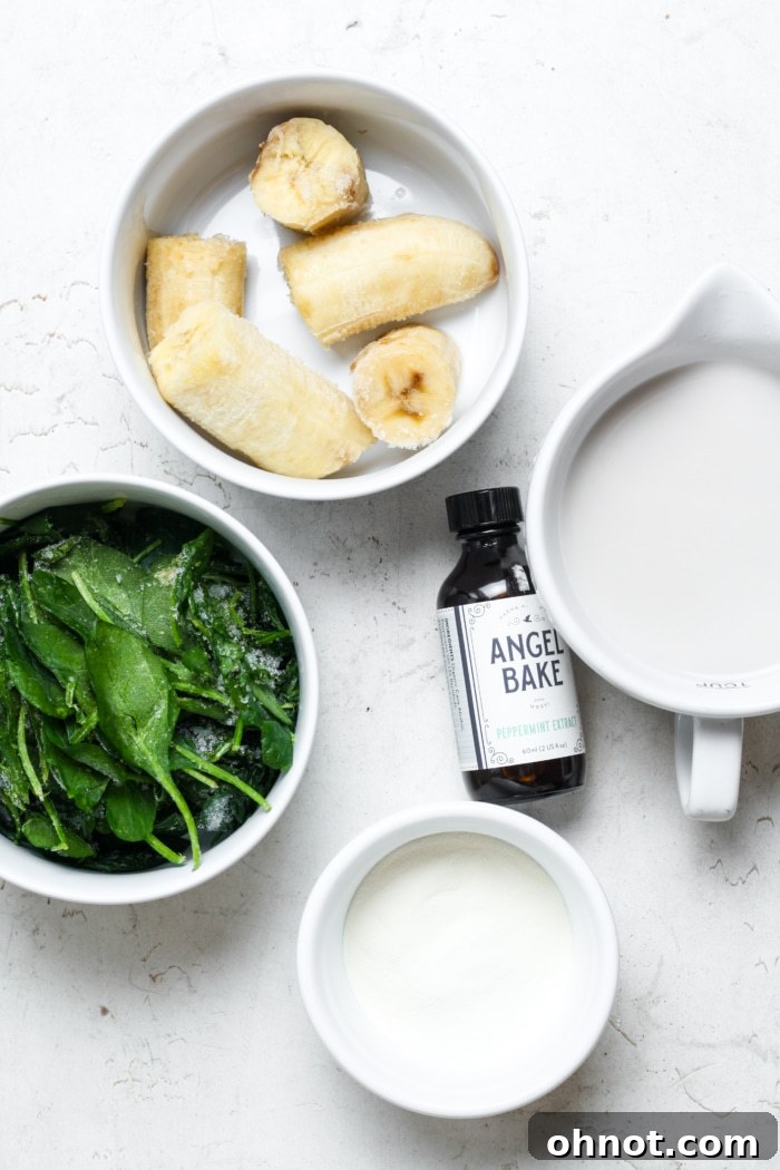 Collection of fresh ingredients for a healthy protein shamrock shake, including frozen banana, spinach, milk, peppermint extract, and protein powder.