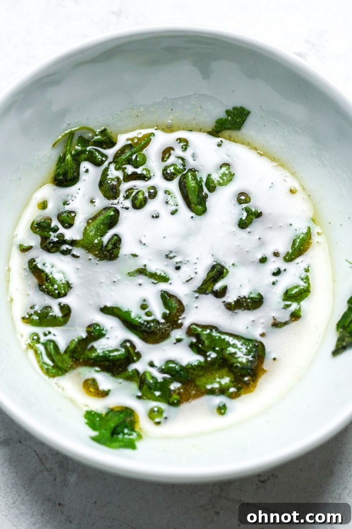 A small bowl of melted herb butter, ready to be brushed onto smashed sweet potatoes.