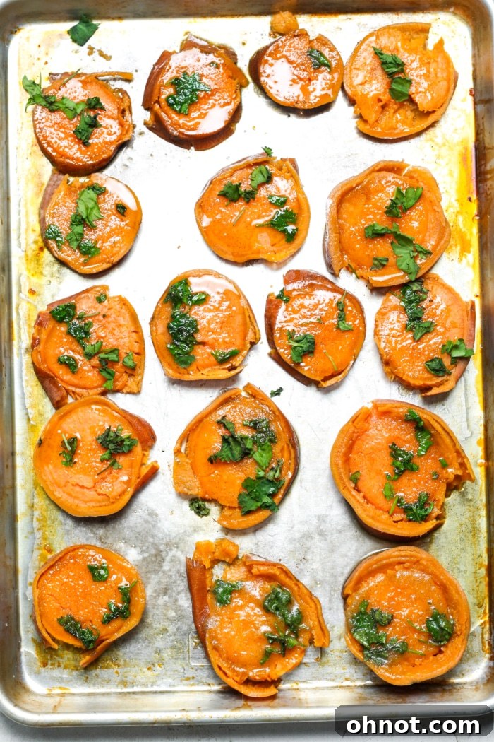 Smashed sweet potato rounds brushed with herb butter on a baking sheet.