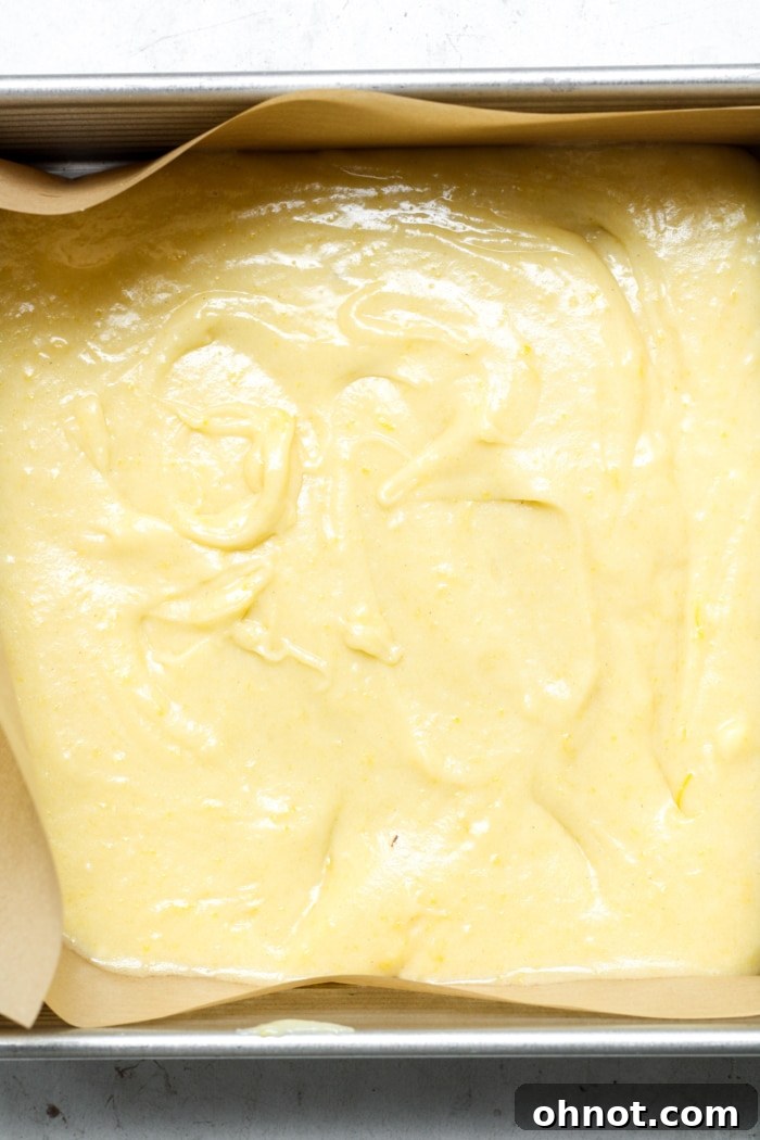 Smooth yellow batter spread evenly in a square baking pan, ready for the oven.