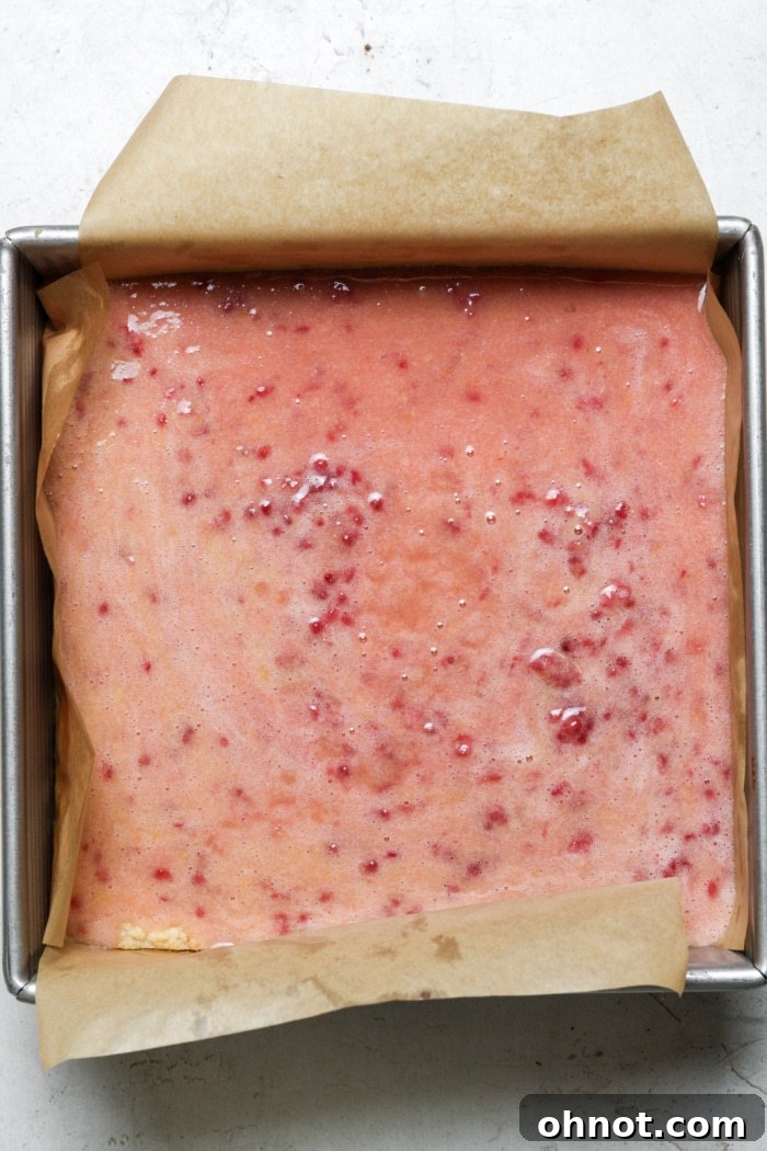 Light pink raspberry lemon filling poured over baked shortbread crust in a pan.