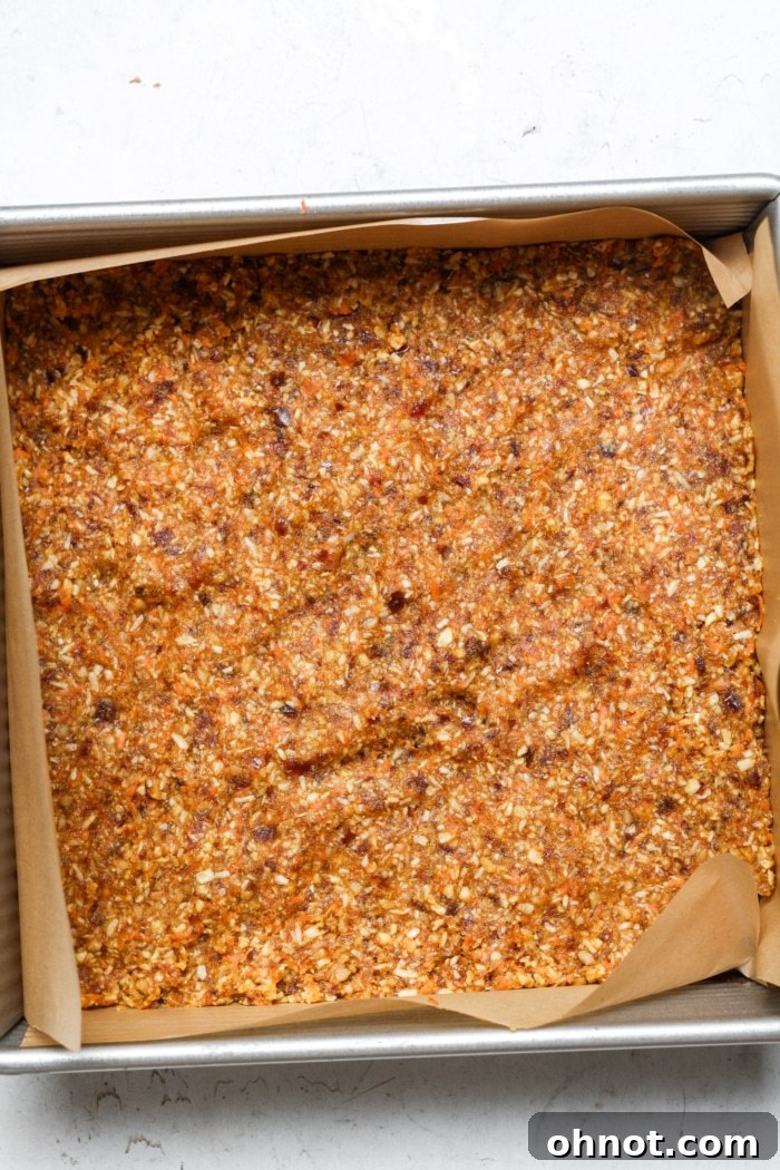 A layer of carrot-based crust pressed evenly into a square baking pan.