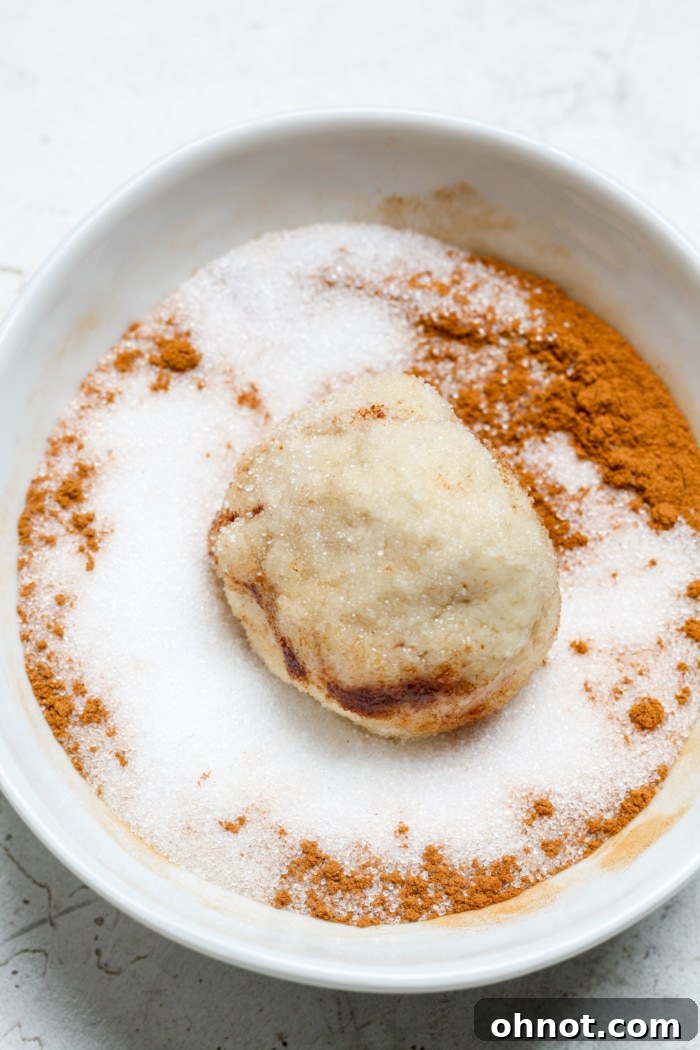 A small ball of dough being coated in cinnamon sugar.