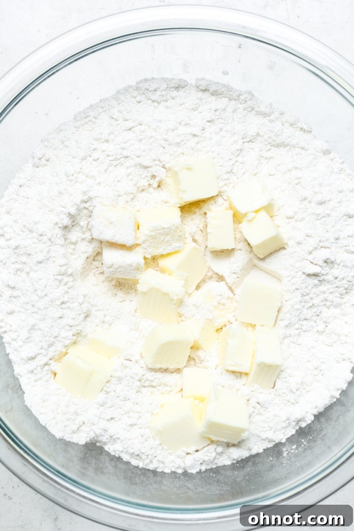 Cold cubed butter being worked into dry ingredients in a bowl.