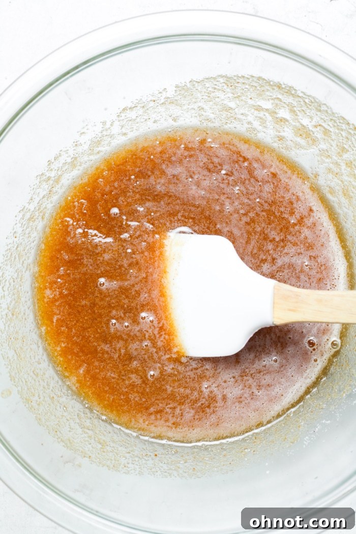 Golden brown butter mixture in a bowl with sugars, being stirred.