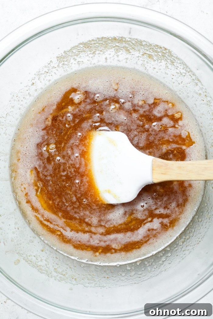 Creamy buttery sugar mixture with egg and vanilla extract, being stirred.