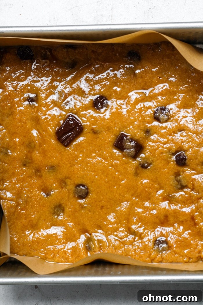 Chocolate chip dough evenly spread in a parchment-lined baking pan.