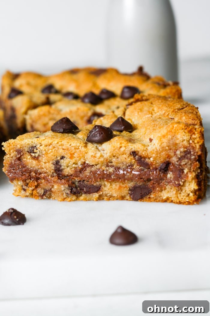 A perfectly baked, warm chocolate chip cookie pie, garnished with a dusting of powdered sugar and ready to be sliced, showcasing its gooey chocolate hazelnut center.