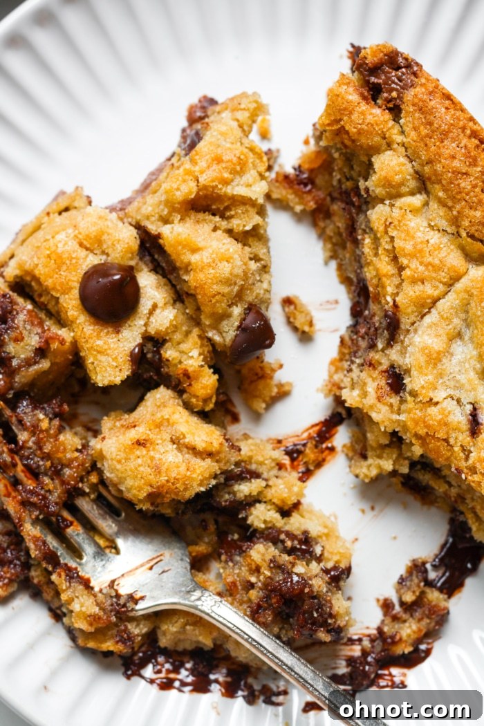 A delicious slice of chocolate chip cookie pie with a fork, showing the rich, melted chocolate hazelnut center on a white plate.