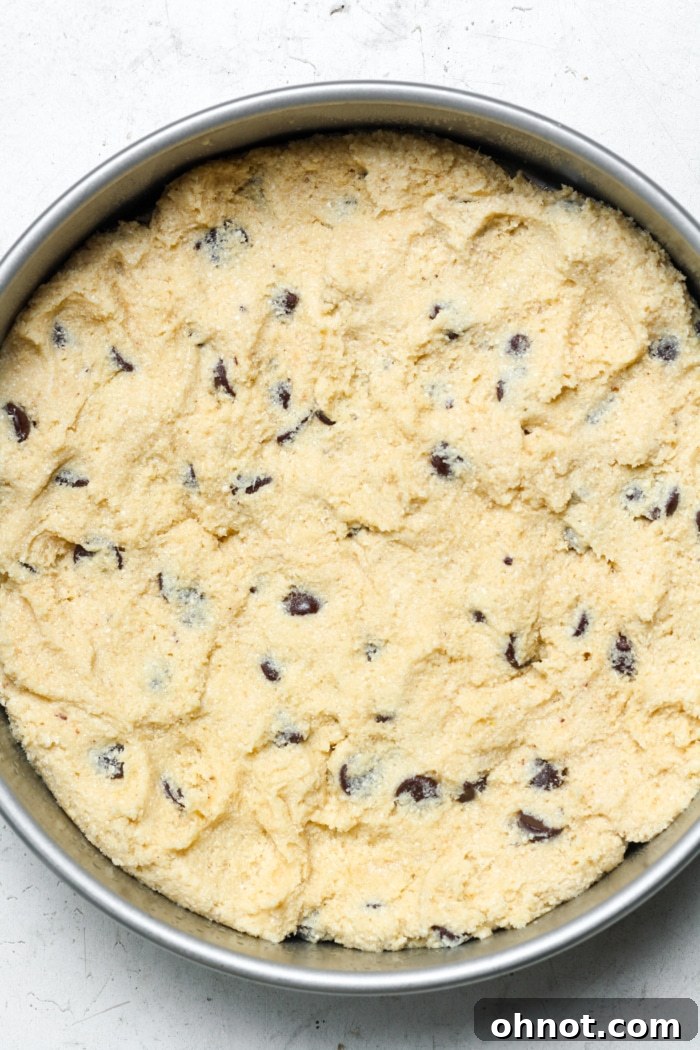A smooth, even layer of chocolate chip cookie dough pressed into an 8-inch round cake pan, forming the base of the pie.