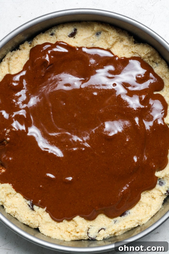 A thick layer of chocolate hazelnut spread (Nutella) spread over the base cookie dough in a cake pan, leaving a small border around the edges.