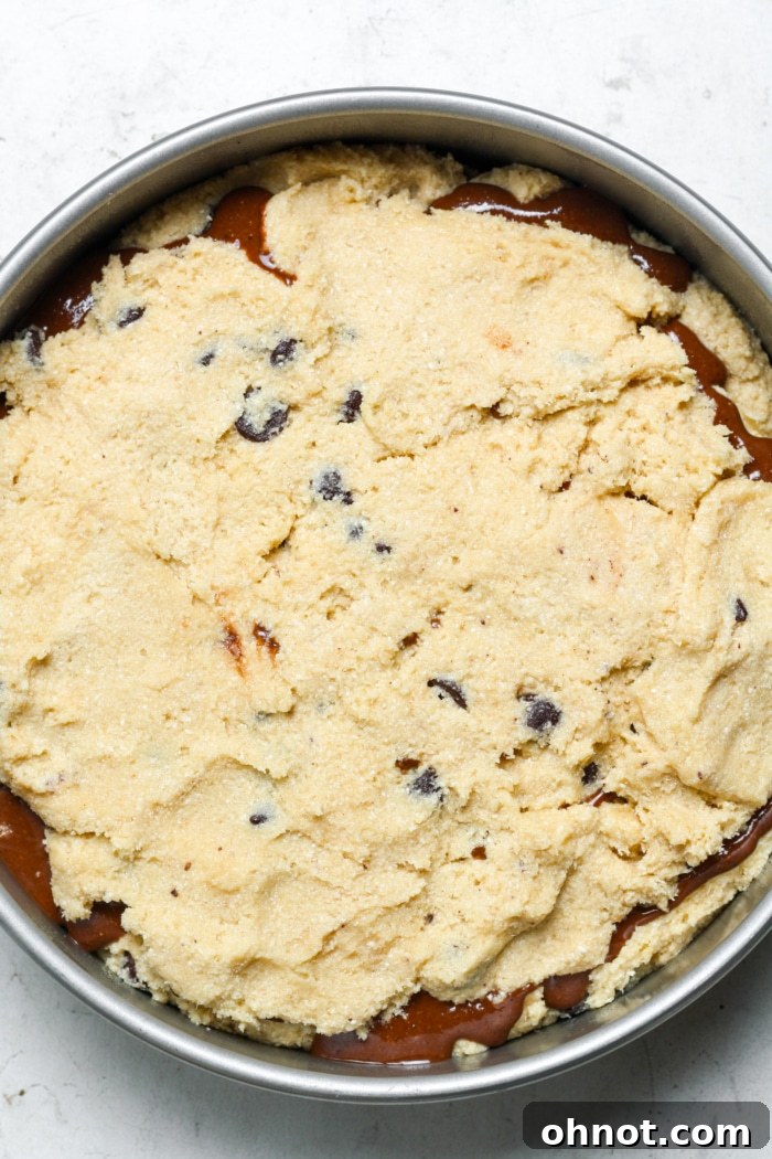 The second layer of chocolate chip cookie dough carefully spread over the chocolate hazelnut filling in the cake pan, enclosing the gooey center.