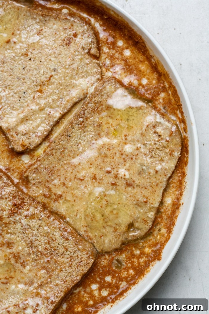 A slice of gluten-free bread being carefully dipped into the creamy egg and milk mixture.