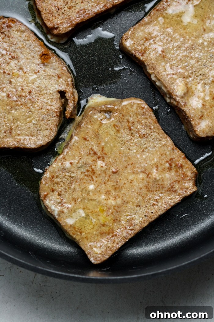 Slices of gluten-free bread cooking in a buttered nonstick skillet, beginning to turn golden.