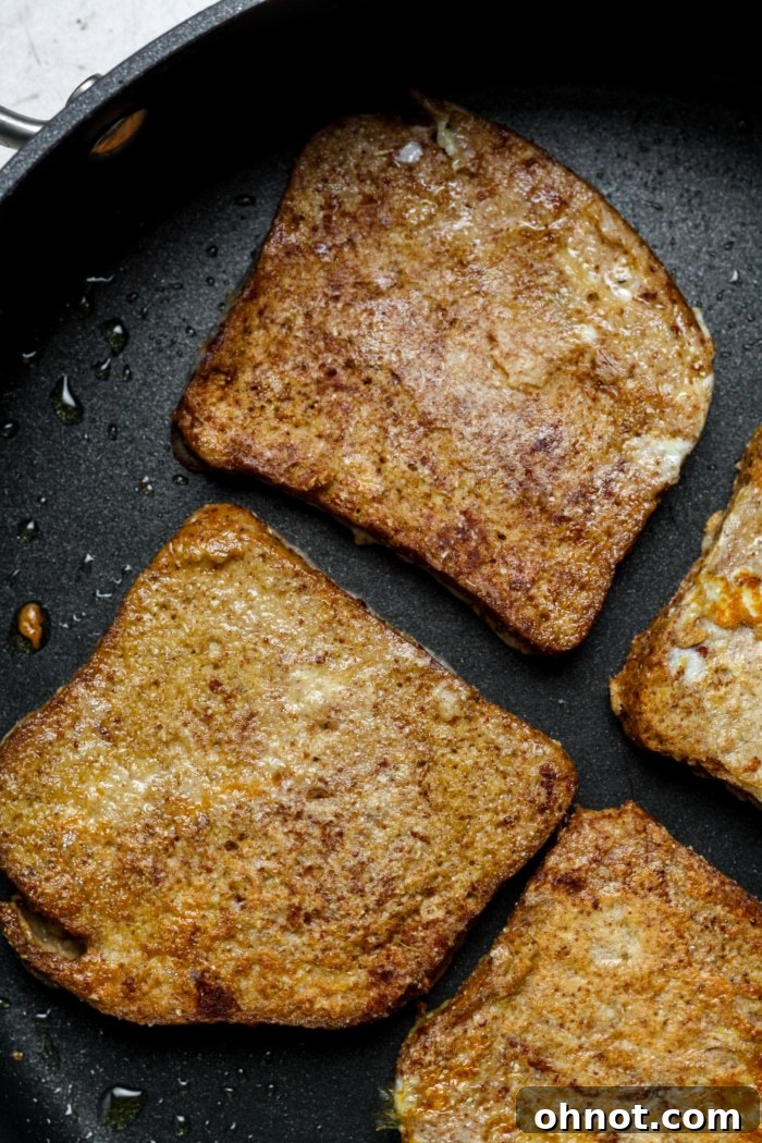 Two slices of seared gluten-free French toast, showcasing their beautiful golden-brown finish in a skillet.