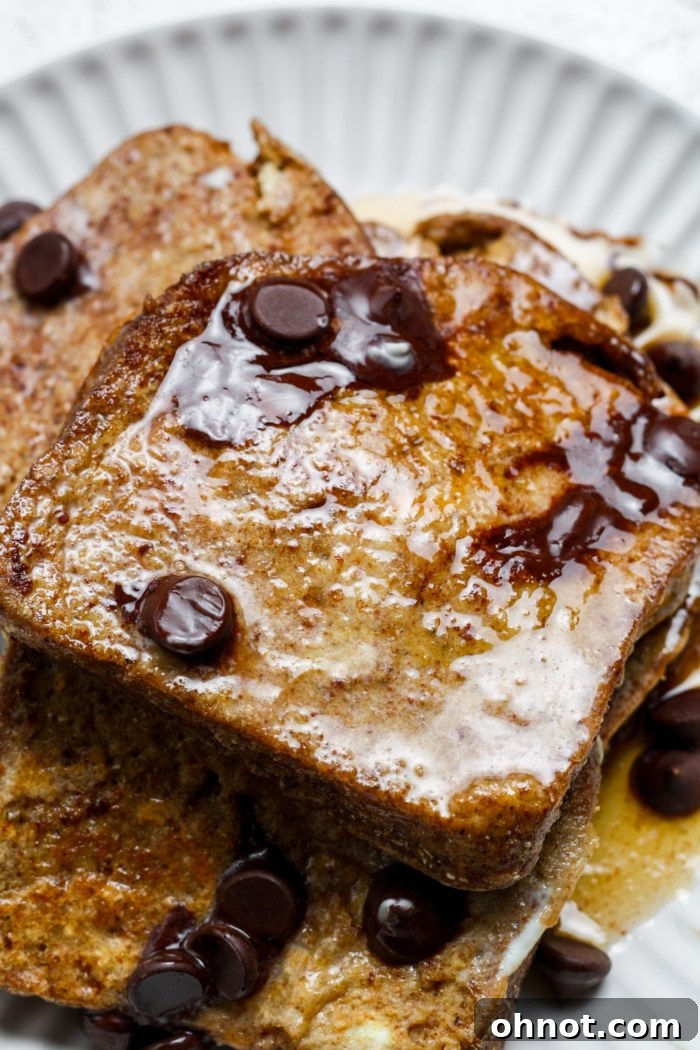 Stacked slices of gluten-free French toast, topped with a pat of butter and drizzled with golden maple syrup.