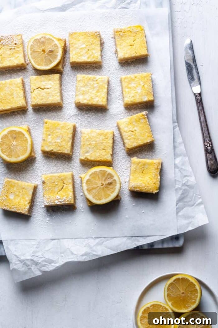Paleo Lemon Bars on a marble slab with a silver knife, showcasing their golden-yellow filling and delicate crust.