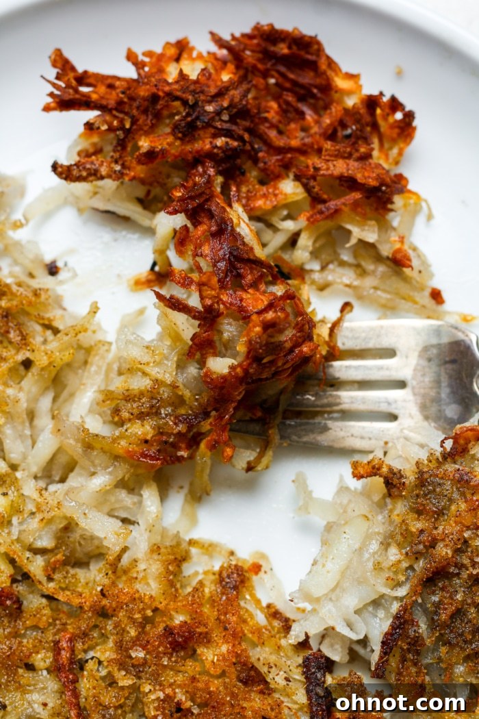 Close-up of a fork lifting crispy air fried hash browns.
