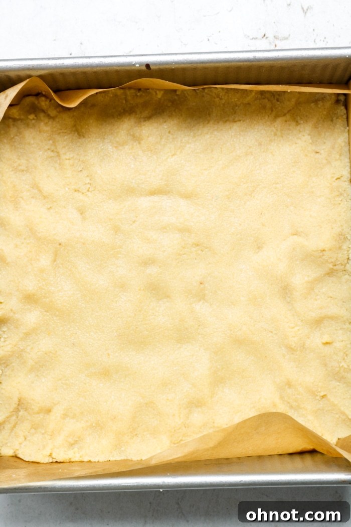 Shortbread base pressed evenly into a square pan, ready for baking.