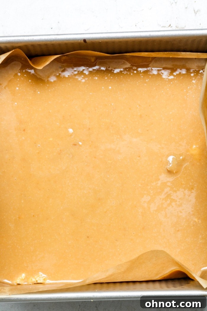 Gooey caramel being poured over the baked shortbread crust in the pan.