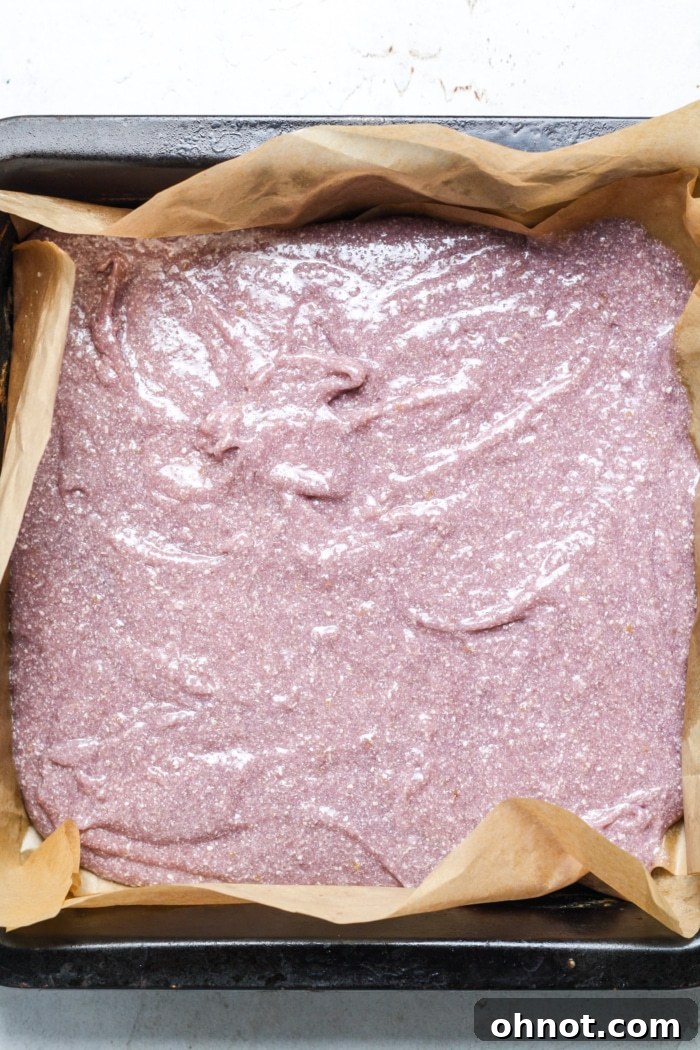 Vibrantly purple ube brownie batter evenly spread in a square baking pan lined with parchment paper.