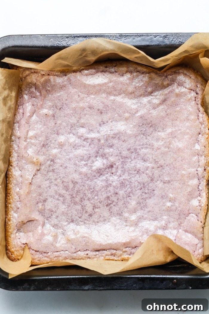 Freshly baked ube brownies cooling in a square pan, showing their beautiful purple color and crinkly top.