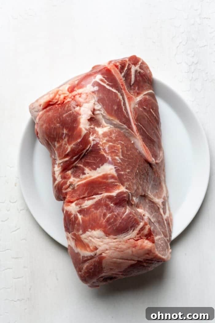 Bone in pork shoulder on a white plate, showcasing the ideal cut for carnitas.