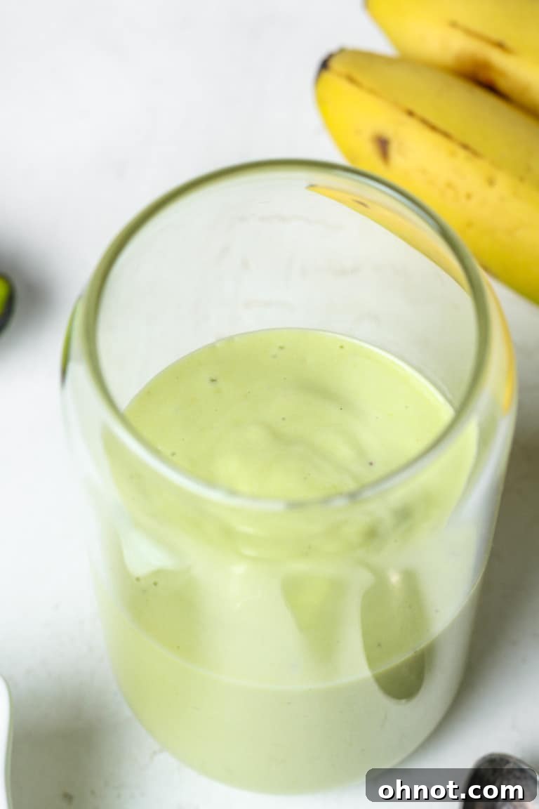 A tall glass of creamy avocado banana smoothie, garnished with a slice of banana.