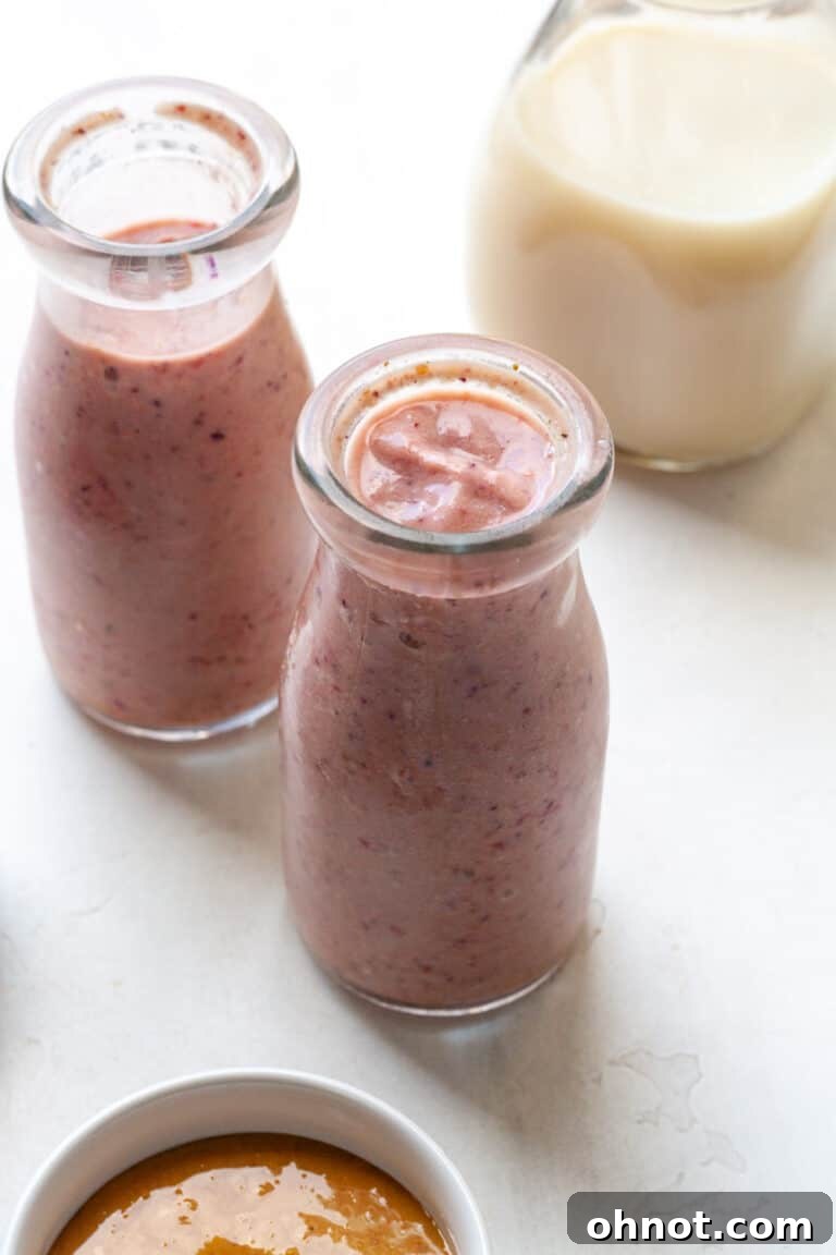 A tall glass of creamy oat milk smoothie garnished with a strawberry.