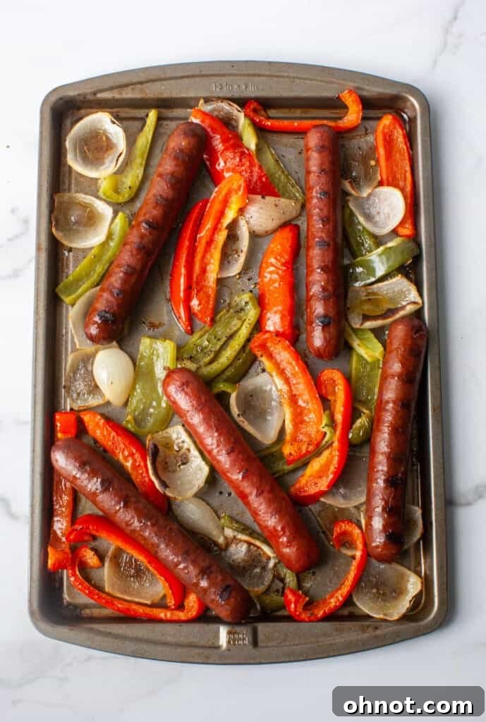 Close-up shot of uniformly chopped red and green bell peppers and sliced onions seasoned with olive oil on a baking sheet, ready for roasting.